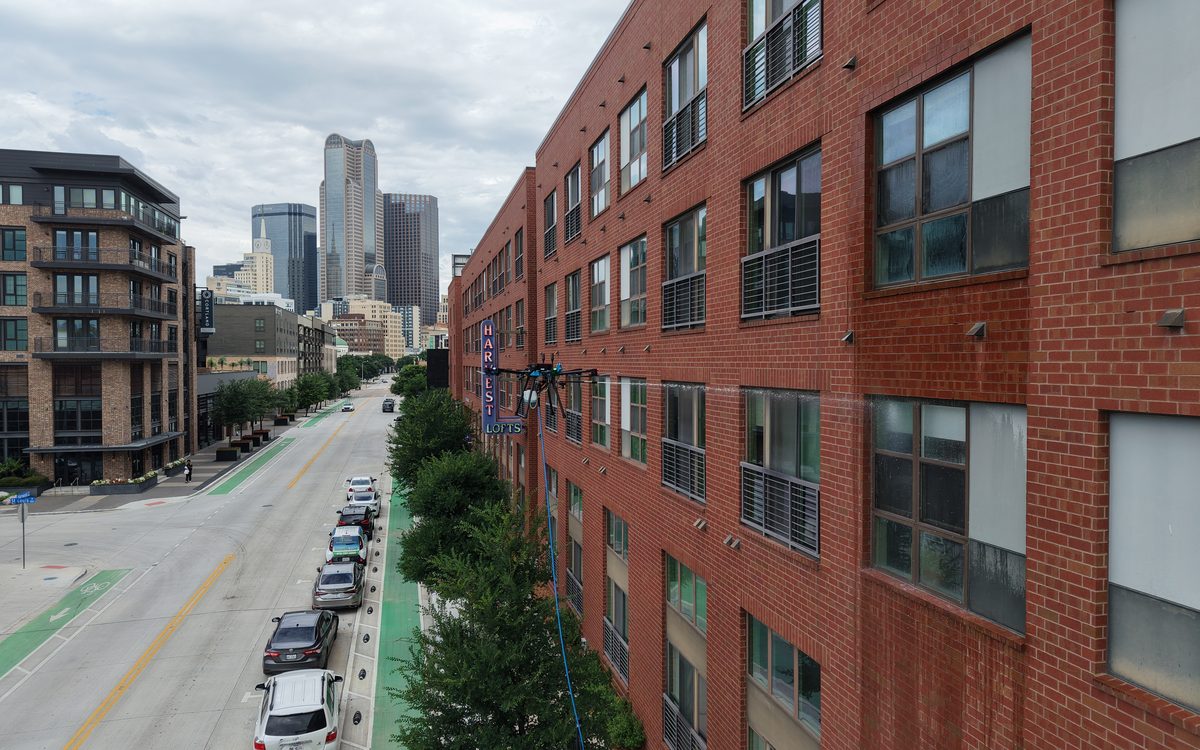 BolAero drone cleaning exterior windows of a four-story brick loft building in the Dallas Farmers Market District, downtown Dallas